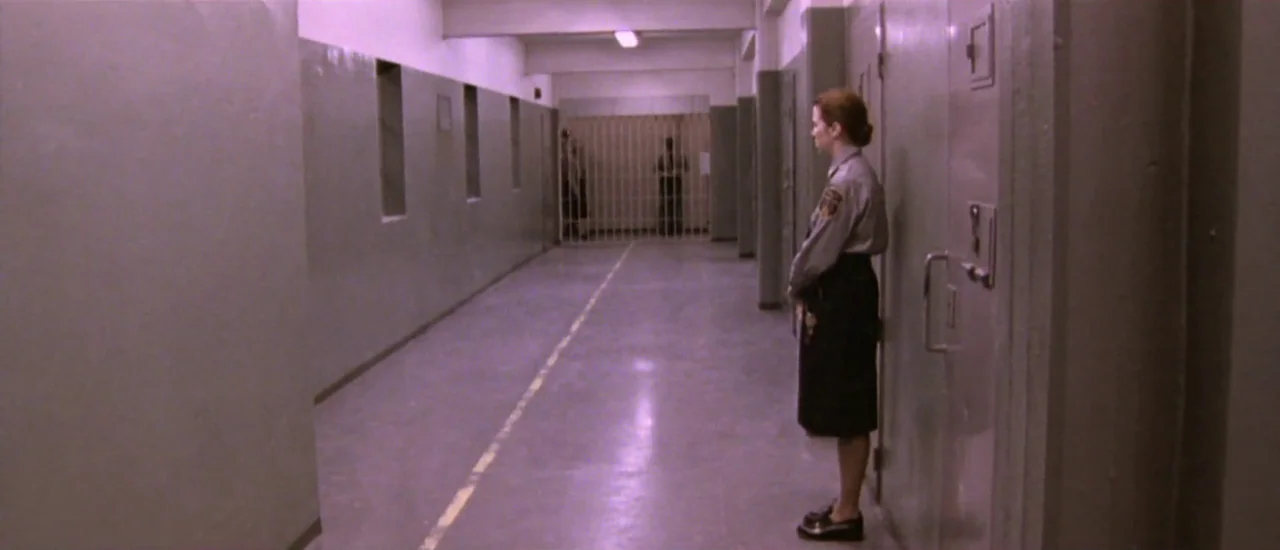 Dancer in the Dark (2000) movie still: wide — A long, sterile institutional hallway features gray metal doors and a barred gate. A female guard…