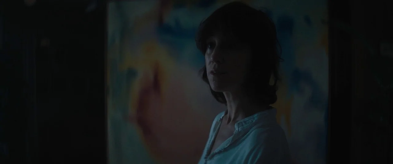 I Think We’re Alone Now (2018) movie still: medium — A dark, dimly lit art studio space is dominated by a large abstract canvas. A woman stands in…