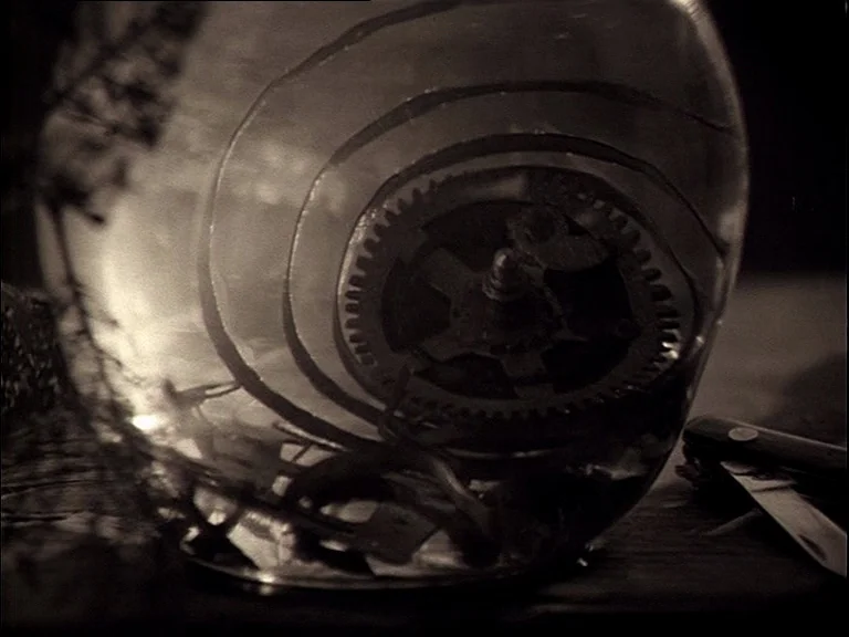 Mirror (Зеркало, Zerkalo) (1975) movie still: closeup — A close view of a metal gear assembly sitting inside a curved glass container. A small…