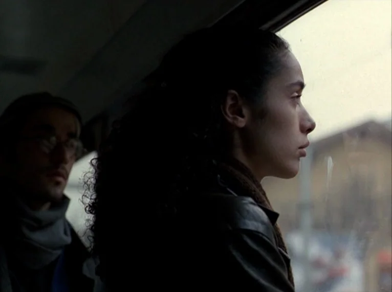 For Ever Mozart (1996) movie still: medium — The interior of a moving passenger train with dark walls and a large window. A young woman gazes…