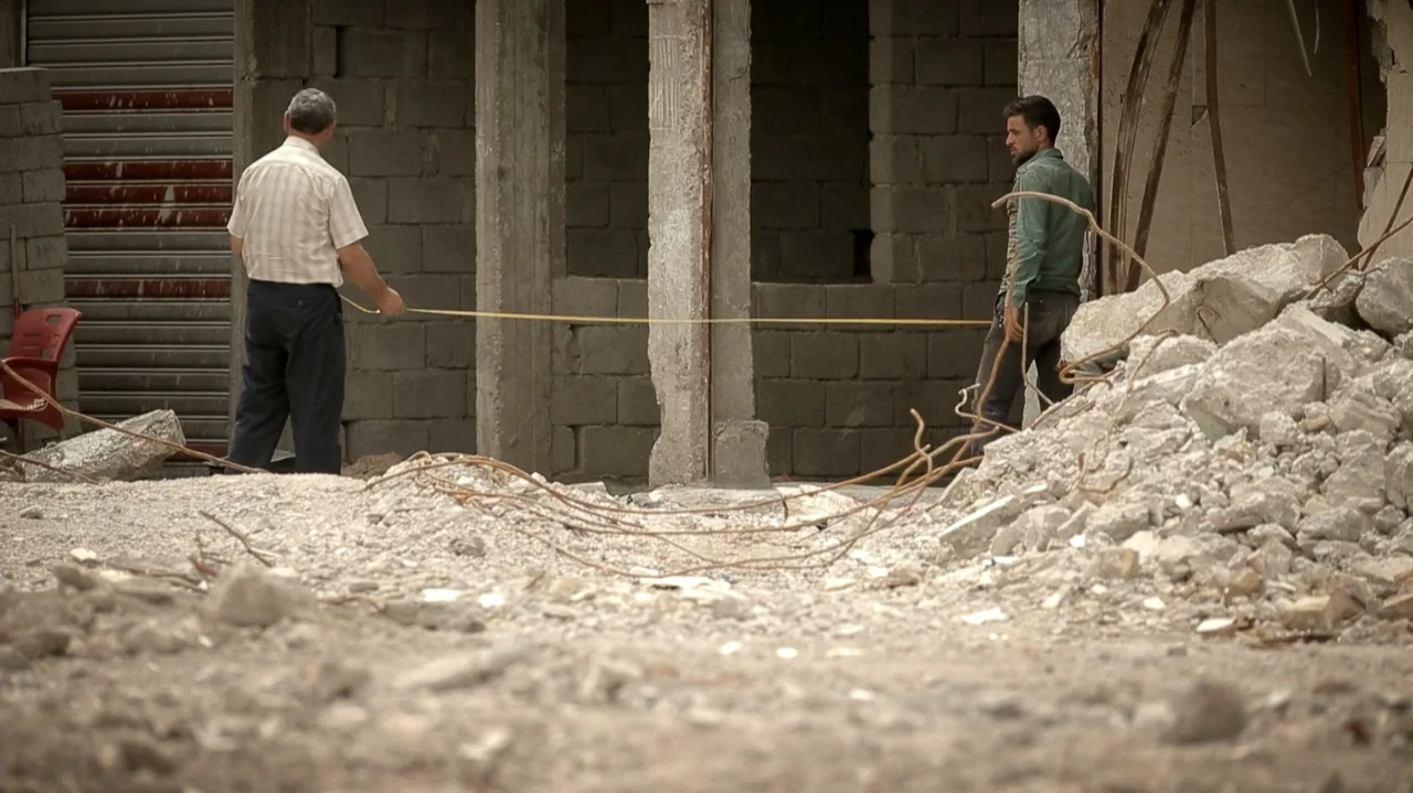 City of Two Springs (2019) movie still: fullbody — A debris-filled construction site features unfinished grey cinder block walls and exposed rebar.…