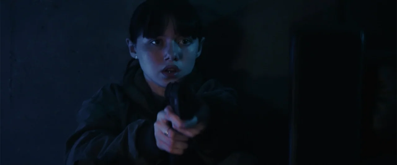 M3GAN 2.0 (2025) movie still: medium — A dimly lit interior space with dark walls obscures the surrounding environment in heavy shadow. A young…