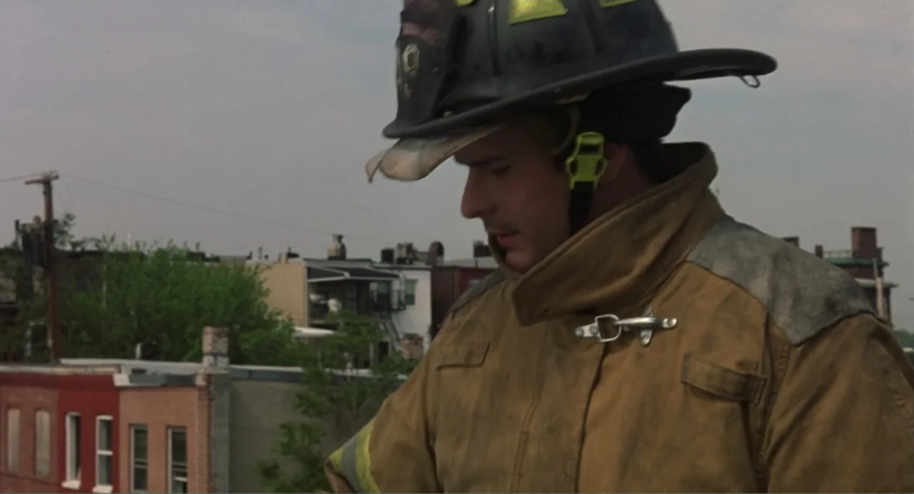 Ladder 49 (2004) movie still: medium — A rooftop overlooks a residential city block with brick row houses in the distance. A firefighter wearing a…
