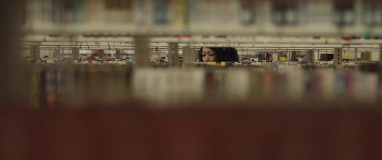 Kumiko the Treasure Hunter (2014) movie still: wide — Rows of bookshelves stretch across the frame, creating blurred foreground and background…