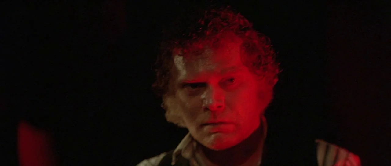 The Funhouse (1981) movie still: closeup — A man stands in a pitch-black space with no other visible features. Harsh red light shines onto his face…