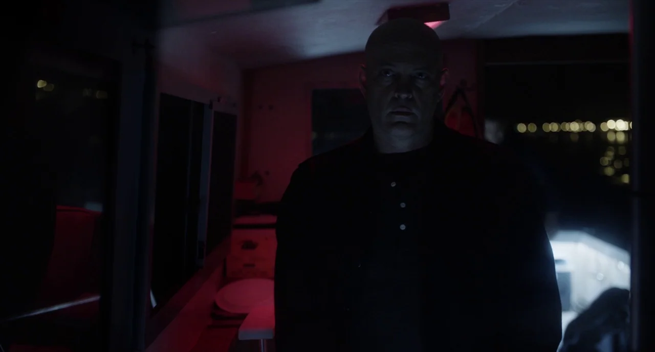 Brawl in Cell Block 99 (2017) movie still: medium — A dark boat cabin is bathed in deep red light from a singular source. A bald man in a dark shirt…