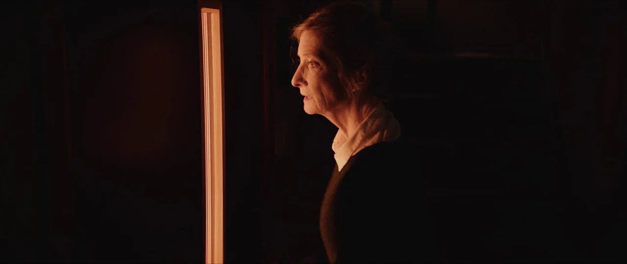Anything For Jackson (2020) movie still: medium — A dark, minimally lit interior space with a single bright, narrow vertical light source. An older…