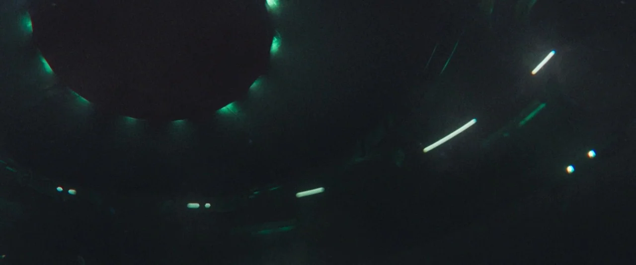 The Vast of Night (2019) movie still: establishing — A dark, curved metallic ceiling features recessed circular and linear green glowing lights. The…