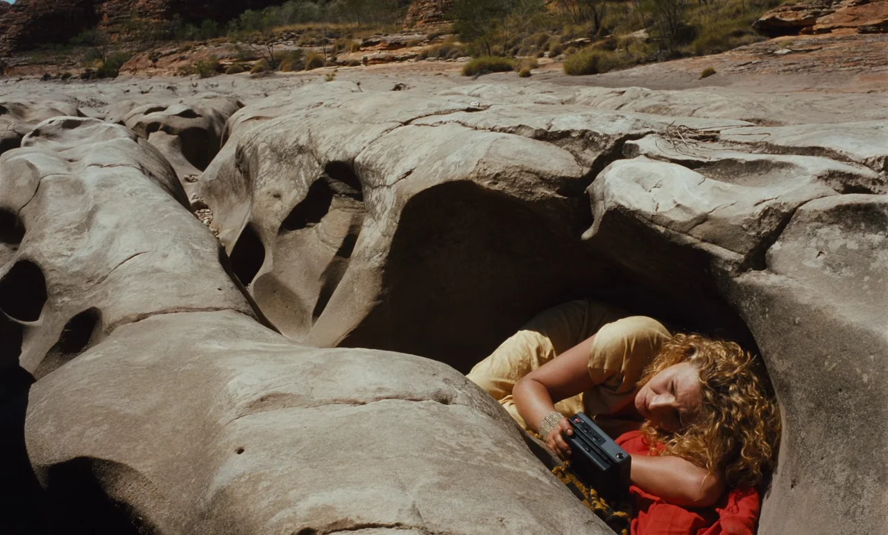 Until The End Of The World (1991) movie still: medium — A woman lies within the smooth, eroded hollow of a tan sandstone rock formation. She rests…