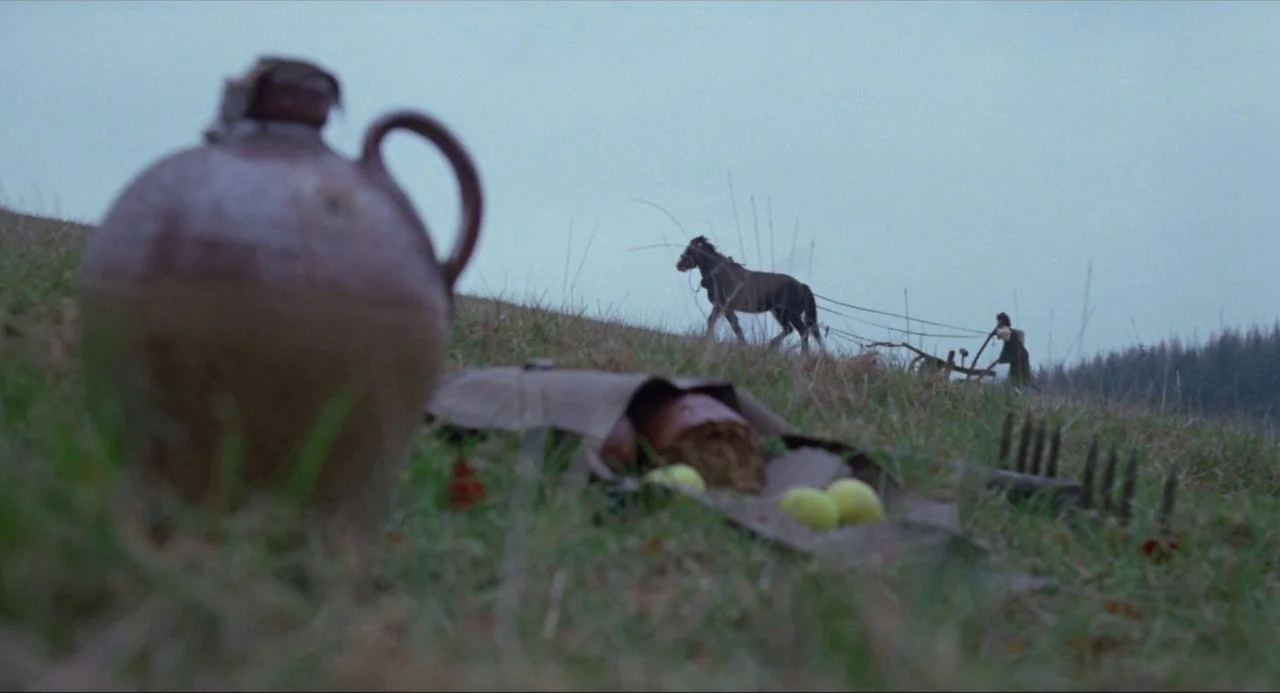 The Blood on Satan’s Claw (1971) movie still: wide — A sloping grassy hill in a rural landscape features a clay jug in the foreground. In the…