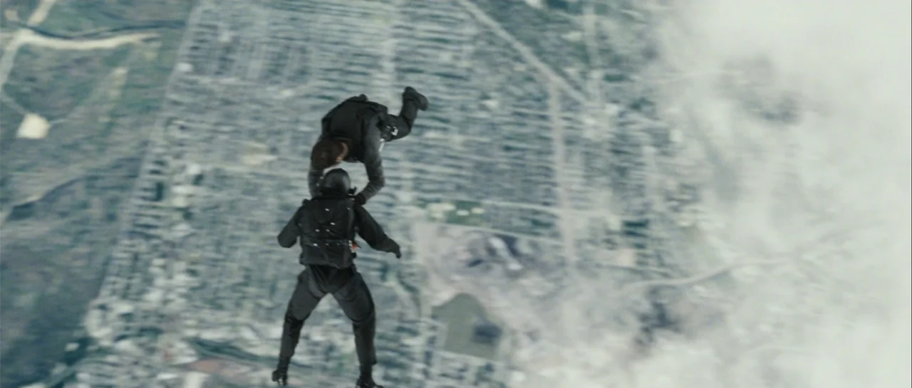 Shoot 'Em Up (2007) movie still: wide — Two individuals in tactical skydiving gear freefall high above a sprawling urban residential area. The…