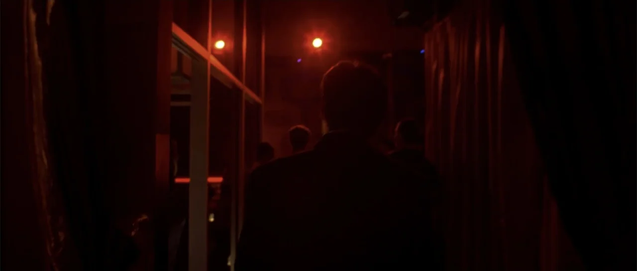 Shade (2003) movie still: medium — A dark corridor leads toward a dimly lit space filled with red light. A man wearing a suit walks away from the…