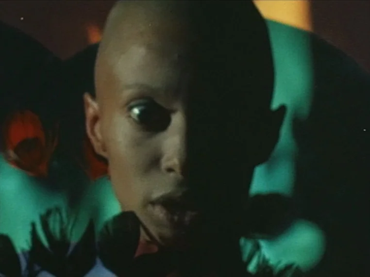 Salome (1972) movie still: closeup — A dark, indistinct space is lit by stark, saturated green neon light sources. A bald person looks toward the…