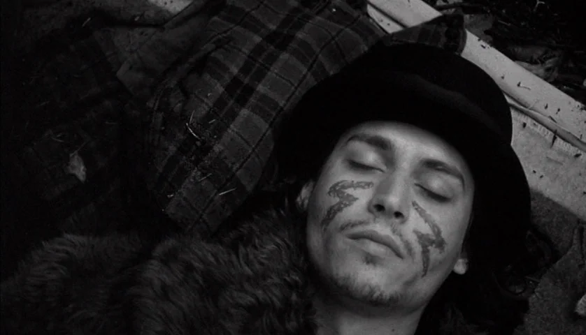 Dead Man (1995) movie still: closeup — A man lies on a rough surface covered by a heavy plaid blanket. He rests with his eyes closed while wearing a…