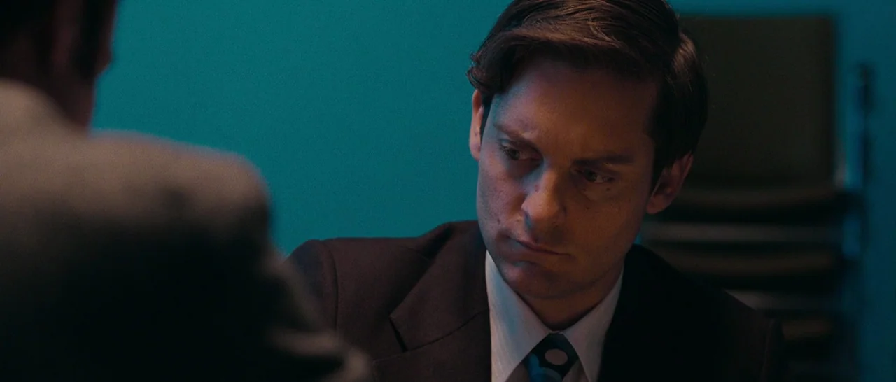 Pawn Sacrifice (2014) movie still: closeup — A man sits at a table in an office against a solid teal-colored wall. He listens while looking down…
