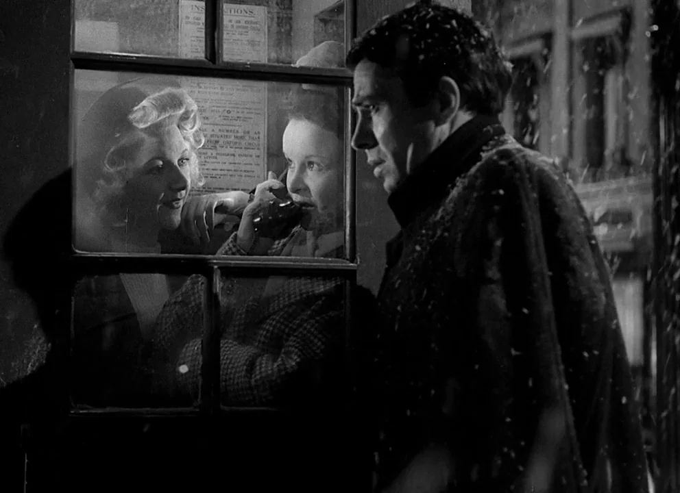 Odd Man Out (1947) movie still: medium — A dark city street at night during a light snowfall with a glass telephone booth. A man in an overcoat…