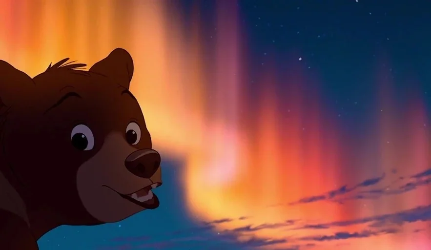 Brother Bear (2003) movie still: closeup — An arctic night sky is filled with vibrant orange and blue aurora borealis lights. A small brown bear cub…