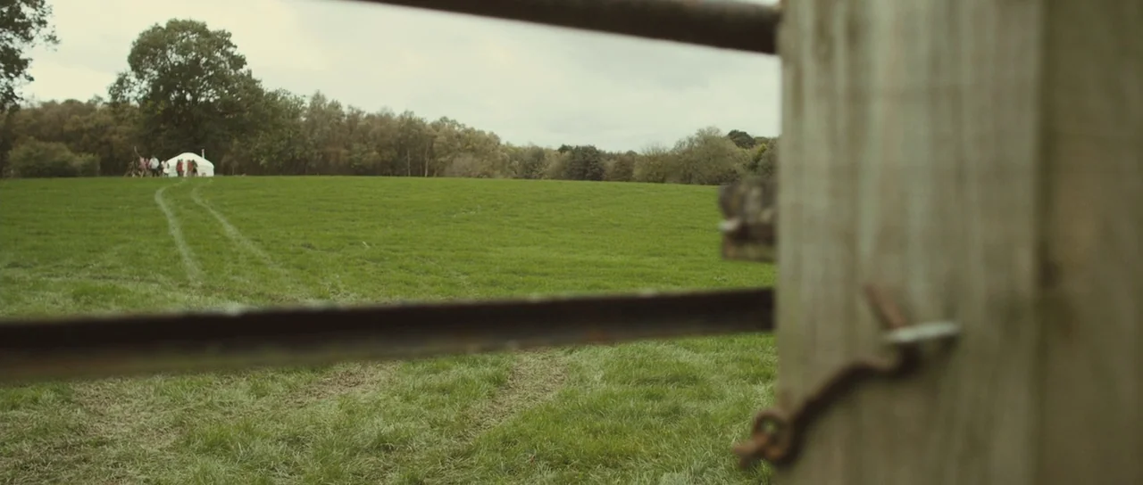Sightseers (2012) movie still: wide — An open green pasture is framed by a blurred wooden gate post in foreground. A small white yurt sits in the…
