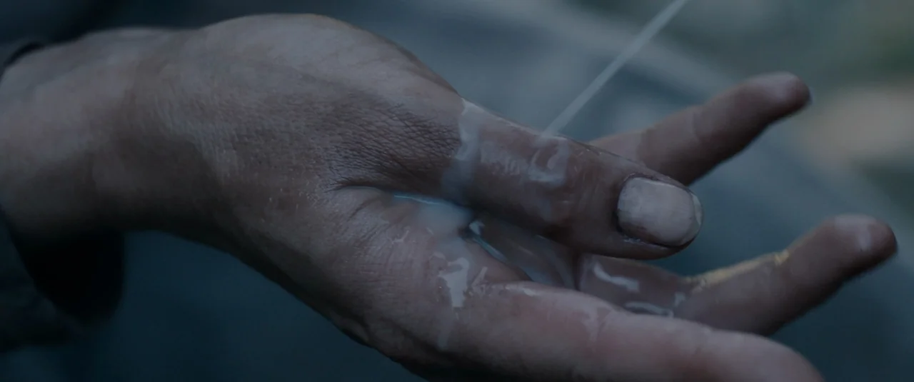 Hagazussa (2017) movie still: closeup — An open human hand is held out in an outdoor setting. White liquid streams down onto the palm and fingers of…