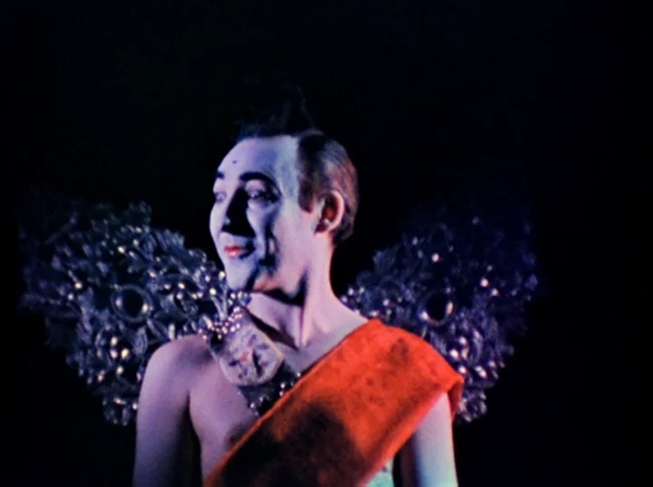 Inauguration of the Pleasure Dome (1954) movie still: medium — A figure in theatrical costume stands before an completely black backdrop. The…
