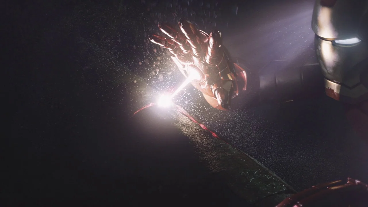 The Avengers (2012) movie still: closeup — A wet asphalt road surface is illuminated by a thin, concentrated beam of light. A robotic figure in gold…