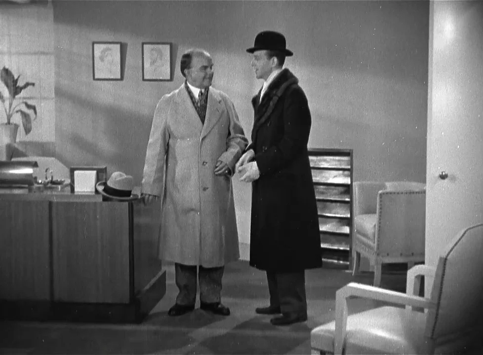 Swing Time (1936) movie still: fullbody — A minimalist, light-toned room features two framed pictures on the wall and chairs. Two men stand in the…