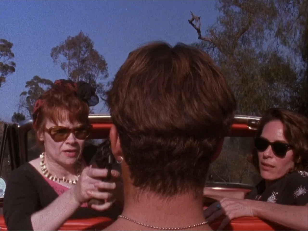 The Living End (1992) movie still: medium — The interior of a red convertible car features three people under bright daylight conditions. One woman…