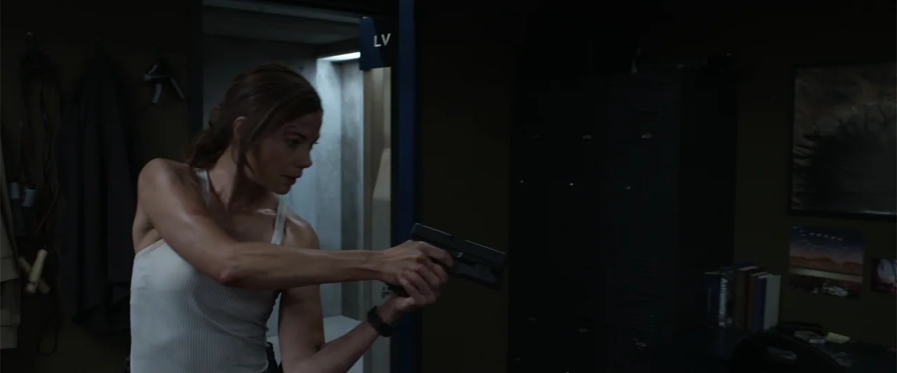 Black Site (2022) movie still: medium — A dimly lit room features black metal lockers and a doorway leading into a shower. A woman in a white tank…