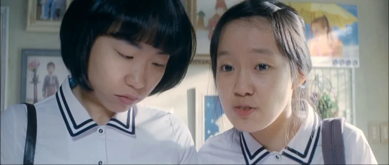 Mother (2009) movie still: medium — A bright indoor space features light-colored walls decorated with various framed photographs and posters. Two…