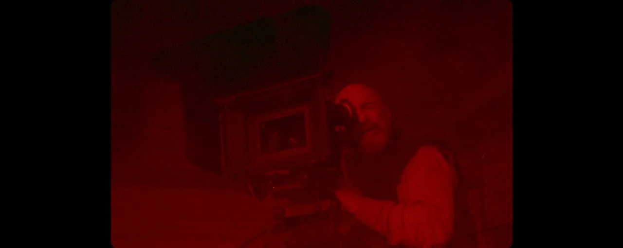 Lux Æterna (2019) movie still: medium — A man operates a professional motion picture camera in a dimly lit, dark space. The subject peers through…