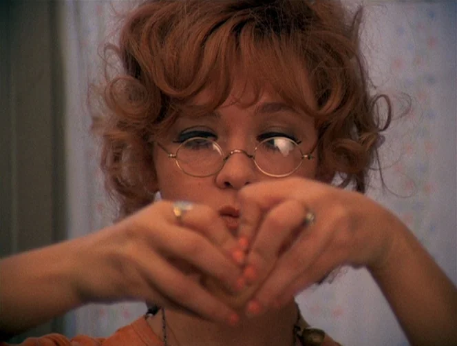 WR: Mysteries of the Organism (1971) movie still: closeup — A close-up shot focuses on a woman in a bathroom with pale patterned walls. She is…