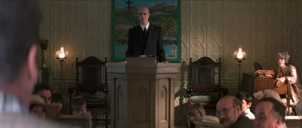 The Pledge (2001) movie still: wide — A small, modest congregation sits on wooden pews facing a simple wooden pulpit. The man at the front gestures…