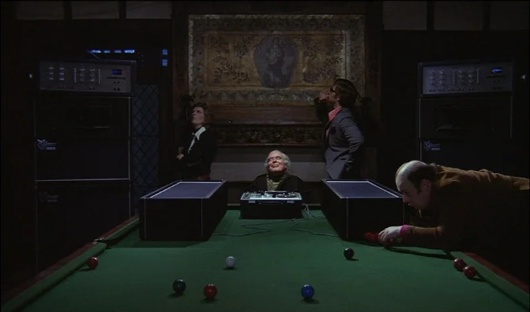 A Clockwork Orange (1971) movie still: wide — A dark billiard room features a green table with scattered balls and audio equipment. Four people…