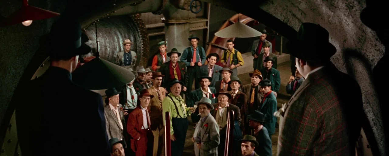 Guys and Dolls (1955) movie still: wide — A dark subterranean space features large metal piping and concrete curved walls. A dense crowd of men in…