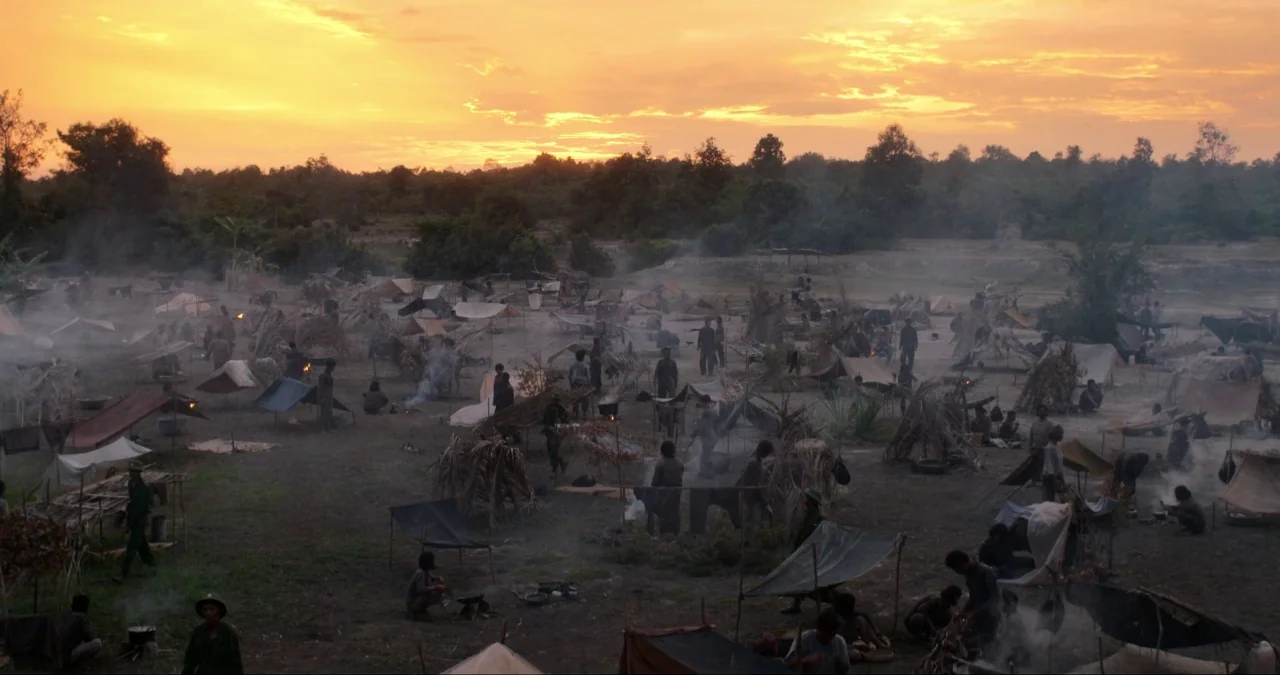 First They Killed My Father (2017) movie still: wide — A vast field serves as a crowded makeshift camp filled with tents and shelters. Smoke rises…