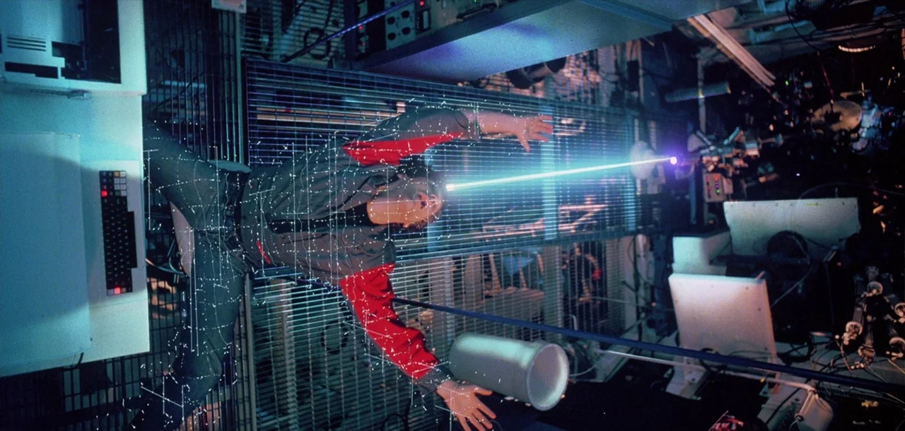 Tron (1982) movie still: medium — A high-tech laboratory interior features metallic grating walls and complex computer equipment. A man in a…