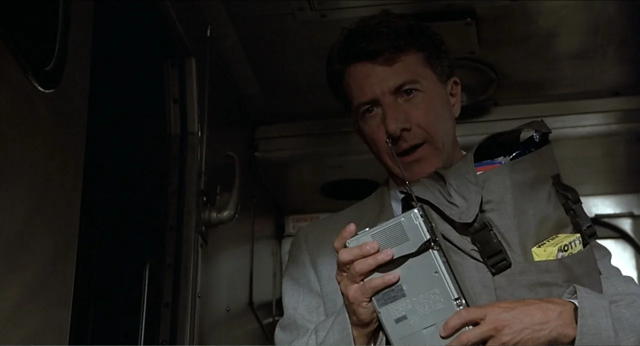 Rain Man (1988) movie still: medium — A dimly lit interior train car with metallic panels and visible door handles. A man in a suit holds a small…