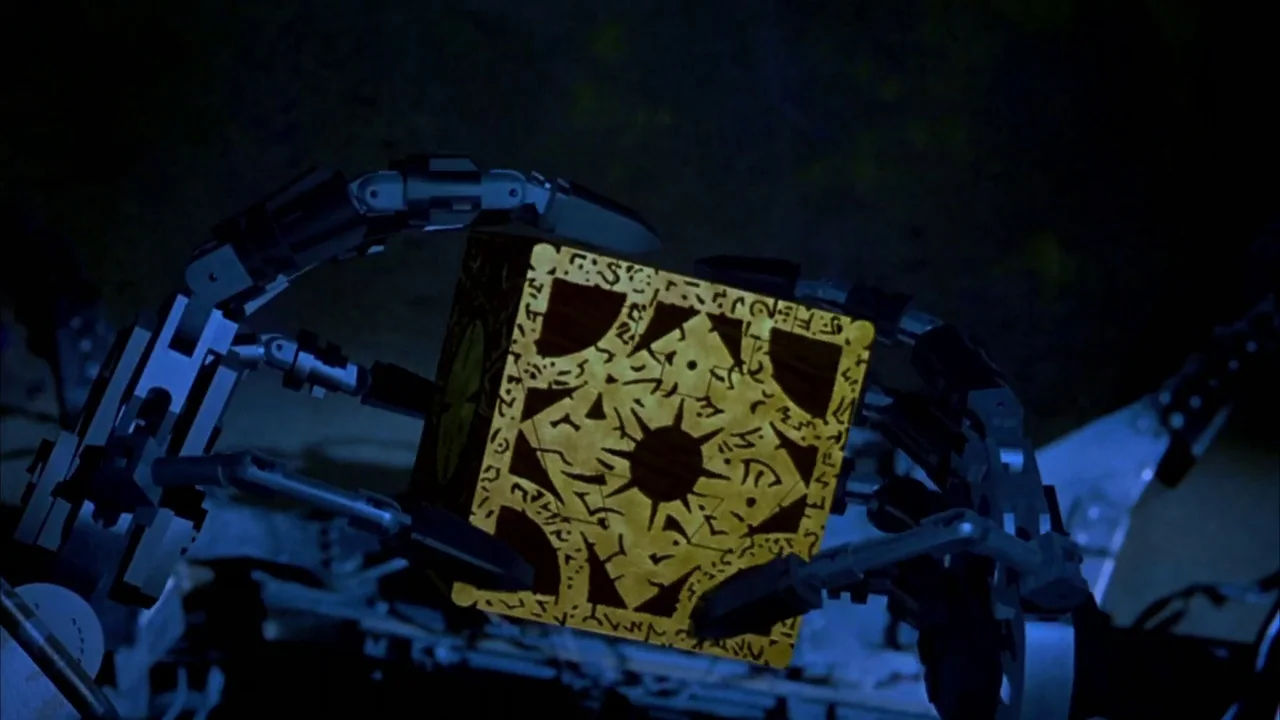 Hellraiser: Bloodline (1996) movie still: closeup — A dark environment contains a mechanical apparatus with articulated arms holding a puzzle box.…
