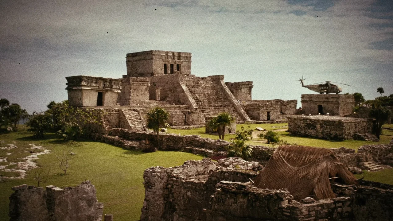 Planet Terror (2007) movie still: establishing — An ancient Mayan stone pyramid stands centered in a grassy coastal archaeological site. A modern…