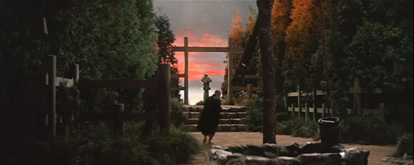 Kwaidan (1964) movie still: wide — A Japanese shrine area features a wooden torii gate and stone stairs at dusk. An elderly man in a dark robe walks…