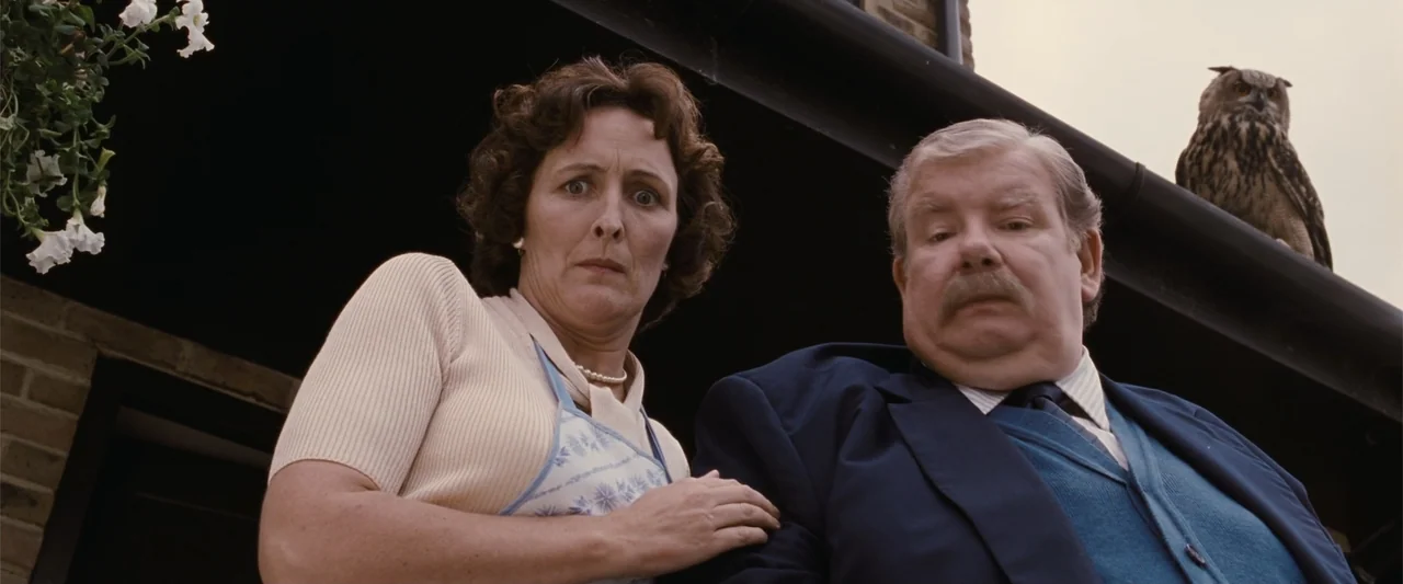 Harry Potter and the Philosopher's Stone (2001) movie still: medium — Two middle-aged people stand on a suburban porch looking down at the camera. A…