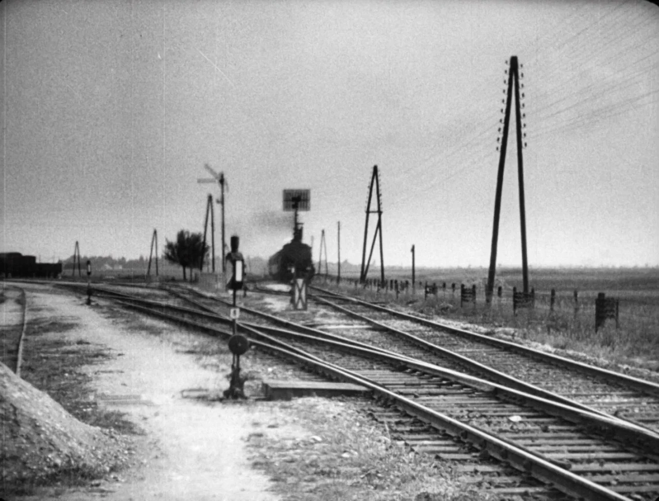 The Hands of Orlac (1924) movie still: wide — An open rural landscape features a network of converging railway tracks. A steam locomotive emits a…