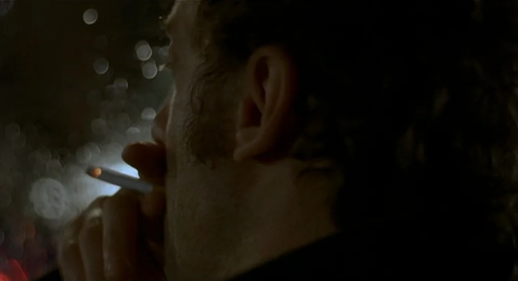 Vendredi Soir (2002) movie still: closeup — A dark, rain-streaked window obscures a city street at night from inside a vehicle. A man sits in…