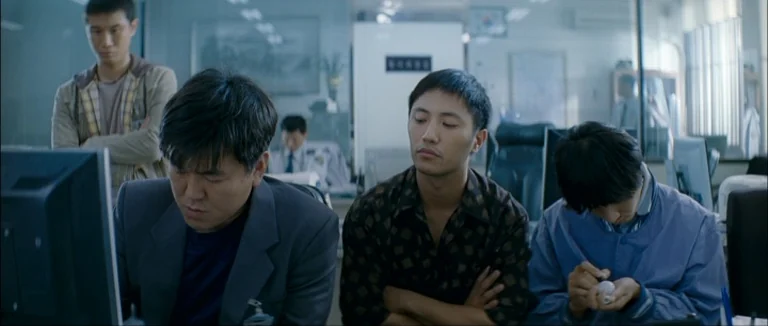 Mother (2009) movie still: medium — An office interior features several men working in a dimly lit, cluttered workspace. The men monitor computers…
