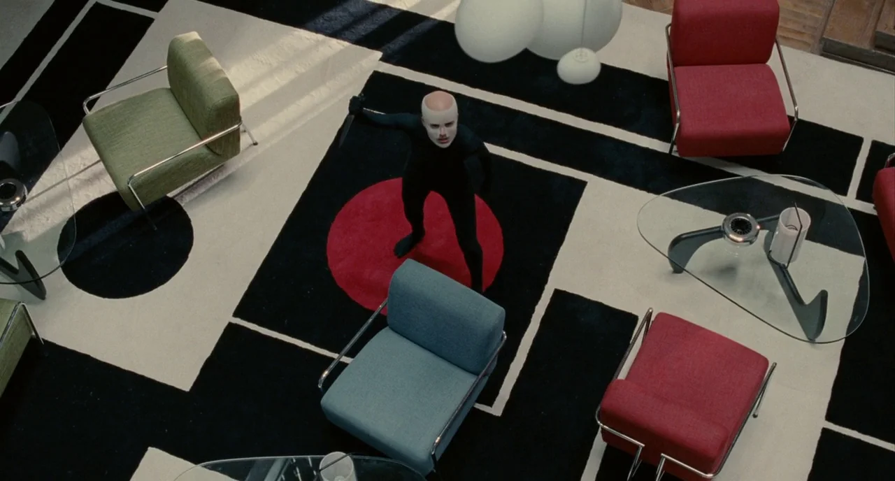 The Skin I Live In (2011) movie still: wide — A spacious room features a patterned rug with sharp geometric black and white squares. A bald person…