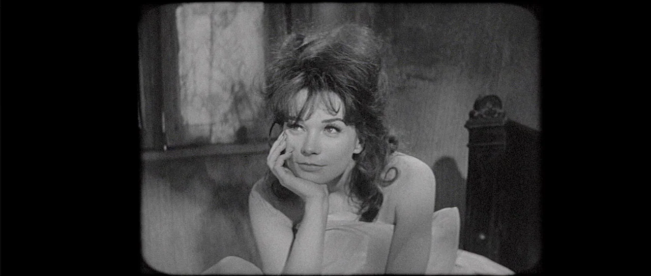 What A Way To Go! (1964) movie still: medium — A woman sits in a bed with a wooden headboard in a dark room. She rests her chin on her hand while…