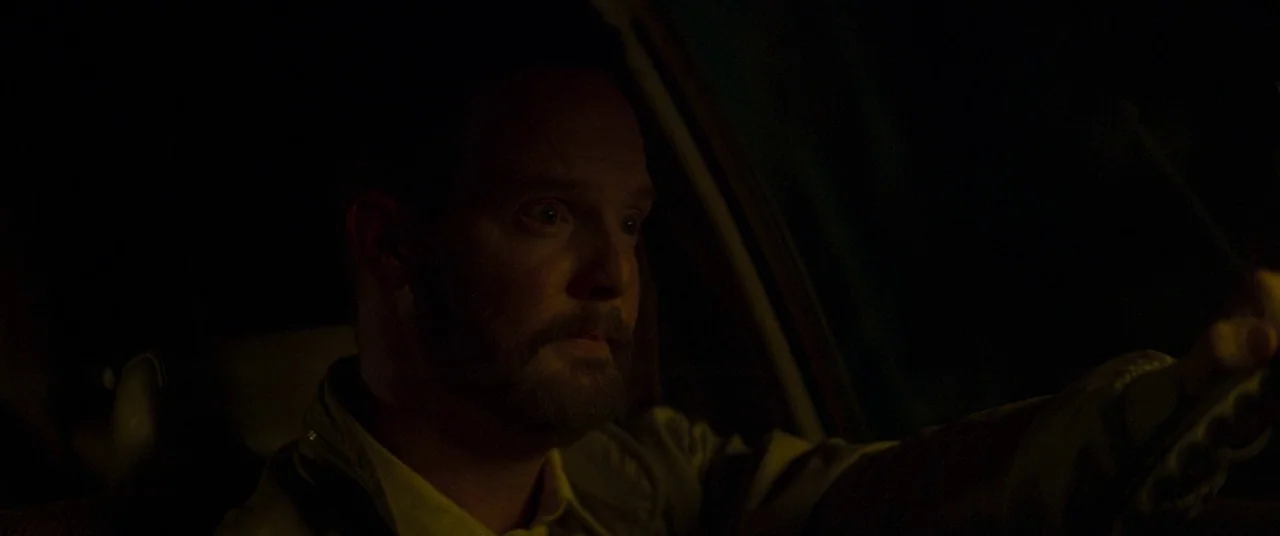 Summer of 84 (2018) movie still: closeup — The interior of a car is dimly lit during the night. A man drives while looking forward with a fixed…