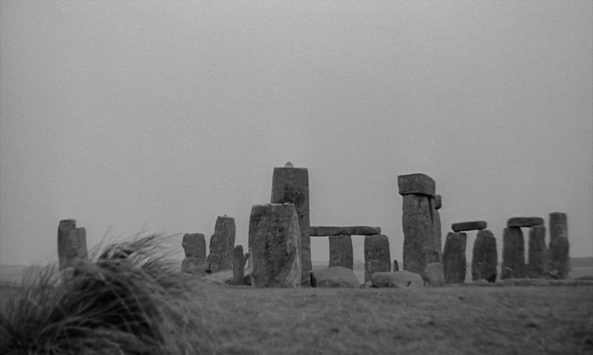 Night Of The Demon (1957) movie still: wide — Stonehenge stands on a grassy plain under an expansive, overcast grey sky. Large weathered megaliths…