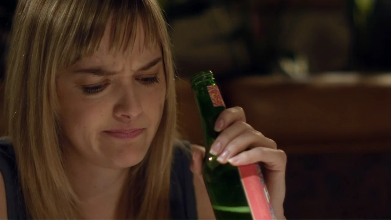 Free Samples (2013) movie still: closeup — A dimly lit indoor bar booth with a warm, out-of-focus background. A blonde woman with bangs stares down…