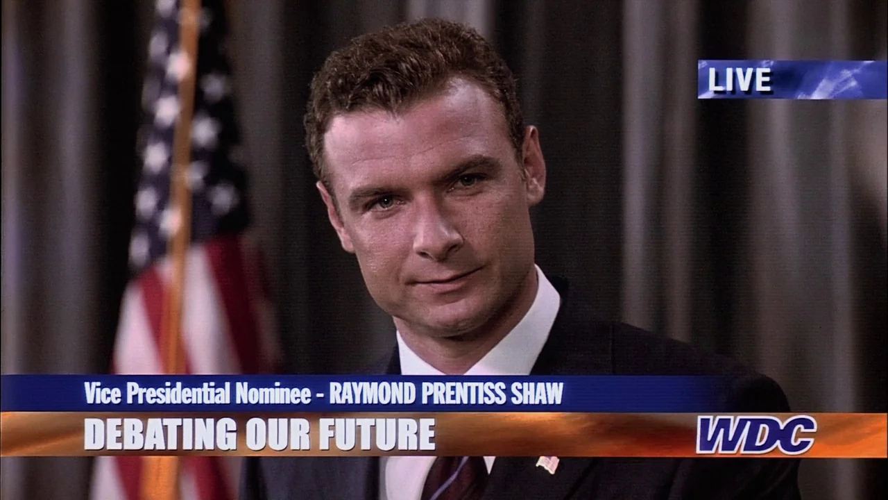 The Manchurian Candidate (2004) movie still: closeup — A man stands before a draped background in a television news studio setting. An overlaid…